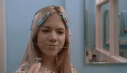 A Woman Is Shaving Her Face With A Razor In Front Of A Mirror In A Bathroom . GIF