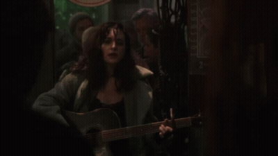 A Woman Is Singing And Playing A Guitar In Front Of A Sign That Says Tuesdays GIF