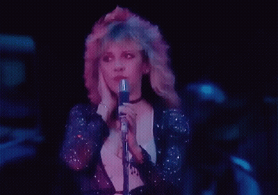 A Woman Is Singing Into A Microphone In A Dark Room . GIF