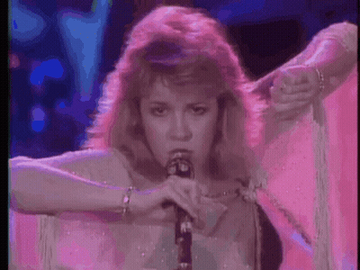 A Woman Is Singing Into A Microphone In A Pink Dress . GIF