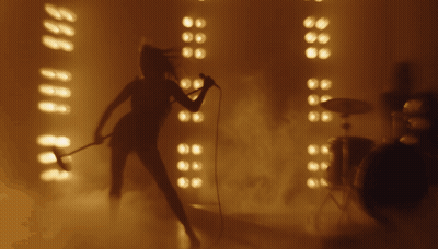 A Woman Is Singing Into A Microphone In Front Of A Drum Set GIF