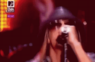 A Woman Is Singing Into A Microphone In Front Of A Mtv Logo . GIF