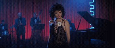 A Woman Is Singing Into A Microphone In Front Of A Piano GIF