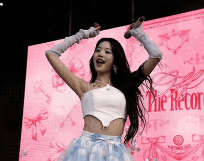A Woman Is Singing Into A Microphone In Front Of A Sign That Says The Record GIF