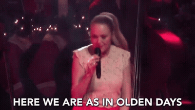 A Woman Is Singing Into A Microphone On A Stage And The Words `` Here We Are As In Olden Days '' Are Behind Her . GIF