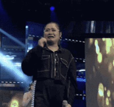 A Woman Is Singing Into A Microphone On A Stage While Crying . GIF