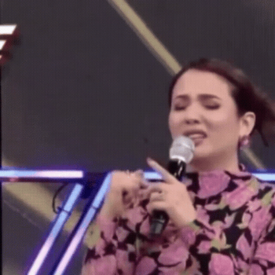 A Woman Is Singing Into A Microphone On A Stage While Making A Funny Face . GIF