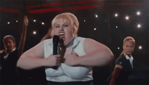 A Woman Is Singing Into A Microphone On A Stage With Other People . GIF