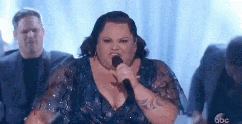 A Woman Is Singing Into A Microphone On Stage . GIF
