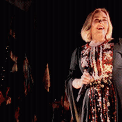 A Woman Is Singing Into A Microphone On Stage GIF