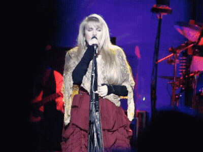 A Woman Is Singing Into A Microphone On Stage GIF
