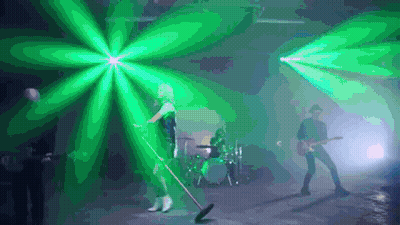 A Woman Is Singing Into A Microphone While A Man Plays A Guitar In A Band . GIF