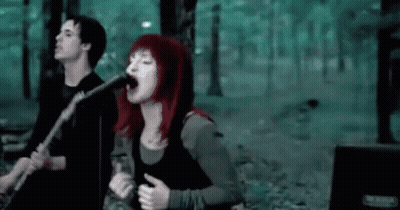A Woman Is Singing Into A Microphone While A Man Plays A Guitar . GIF