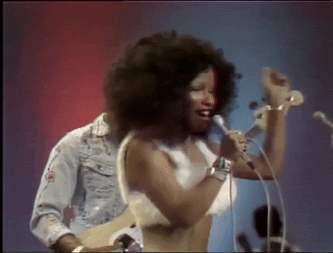 A Woman Is Singing Into A Microphone While A Man Plays A Guitar GIF