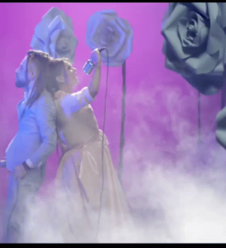 A Woman Is Singing Into A Microphone While A Man Stands Behind Her GIF