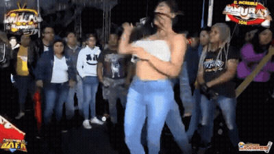 A Woman Is Singing Into A Microphone While Dancing In Front Of A Crowd Of People . GIF