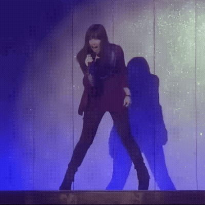 A Woman Is Singing Into A Microphone While Dancing On A Stage . GIF