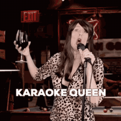 A Woman Is Singing Into A Microphone While Holding A Glass Of Wine And The Words Karaoke Queen Are On The Bottom GIF