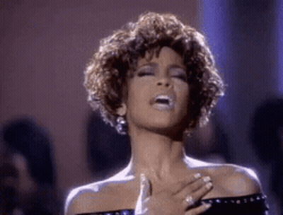 A Woman Is Singing Into A Microphone While Holding Her Hands To Her Chest . GIF