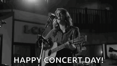 A Woman Is Singing Into A Microphone While Playing A Guitar On A Stage . GIF