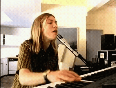 A Woman Is Singing Into A Microphone While Playing A Keyboard In A Living Room . GIF