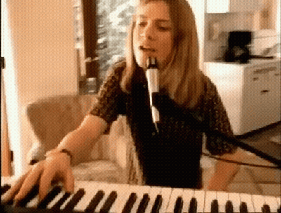 A Woman Is Singing Into A Microphone While Playing A Keyboard GIF
