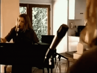 A Woman Is Singing Into A Microphone While Playing A Piano In A Room . GIF