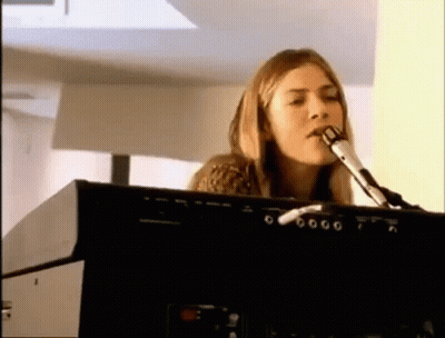 A Woman Is Singing Into A Microphone While Playing An Electronic Keyboard . GIF