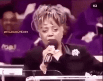 A Woman Is Singing Into A Microphone While Sitting At A Podium In A Church . GIF