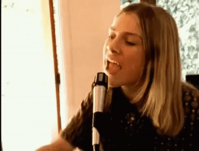 A Woman Is Singing Into A Microphone While Sitting In Front Of A Window . GIF