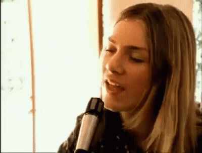 A Woman Is Singing Into A Microphone While Sitting In Front Of A Window . GIF