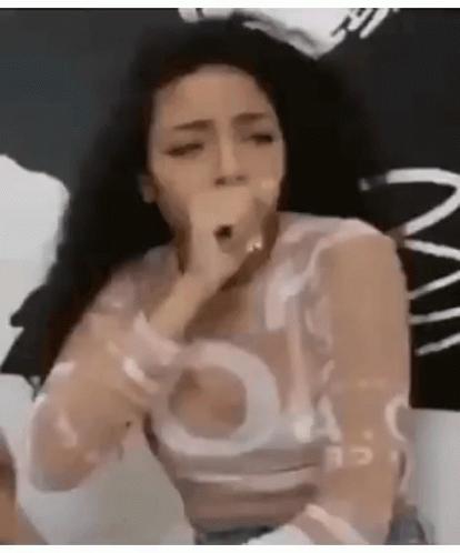 A Woman Is Singing Into A Microphone While Sitting On A Bed In A Room . GIF
