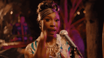A Woman Is Singing Into A Microphone While Sitting On A Stage . GIF