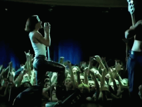 A Woman Is Singing Into A Microphone While Standing On A Stage In Front Of A Crowd . GIF