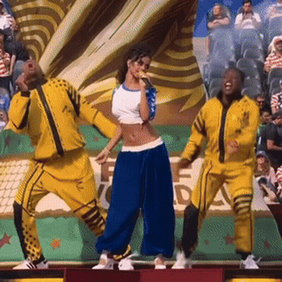 A Woman Is Singing Into A Microphone While Two Men Are Dancing In Front Of A Crowd GIF