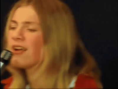 A Woman Is Singing Into A Microphone While Wearing A Red Shirt . GIF