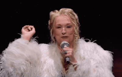 A Woman Is Singing Into A Microphone While Wearing A White Fur Coat . GIF
