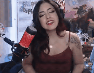 A Woman Is Singing Into A Microphone While Wearing Headphones And A Red Tank Top . GIF