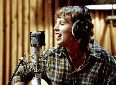 A Woman Is Singing Into A Microphone With Headphones On GIF