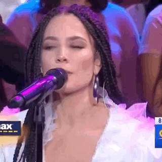 A Woman Is Singing Into A Microphone With Her Eyes Closed In Front Of A Crowd . GIF