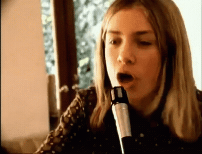 A Woman Is Singing Into A Microphone With Her Mouth Open . GIF