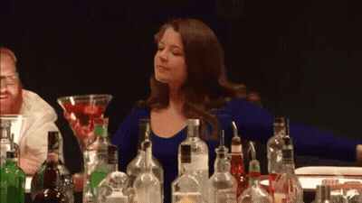 A Woman Is Sitting At A Bar Surrounded By Bottles Of Liquor . GIF
