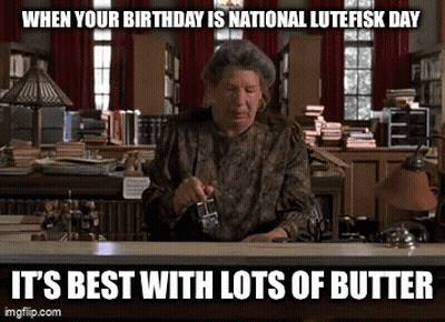 A Woman Is Sitting At A Desk In A Library Holding A Glass Of Butter GIF