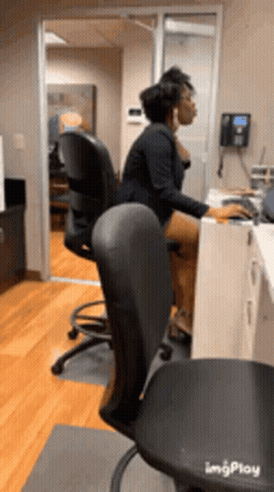 A Woman Is Sitting At A Desk In An Office Using A Computer GIF