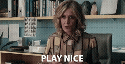 A Woman Is Sitting At A Desk In Front Of A Bookshelf And Saying Play Nice . GIF
