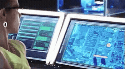 A Woman Is Sitting At A Desk In Front Of Two Computer Monitors . GIF