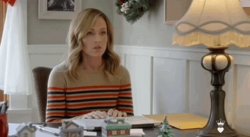 A Woman Is Sitting At A Desk With A Lamp And A Laptop . GIF
