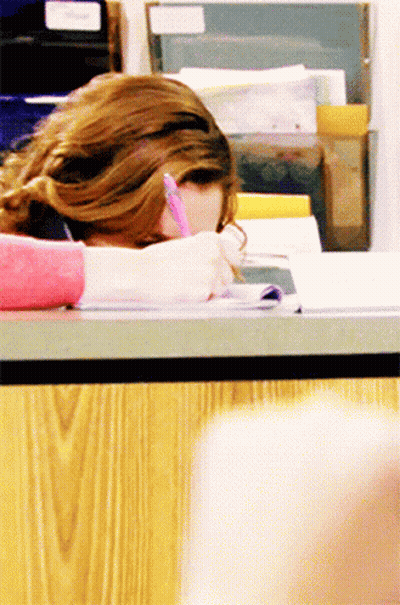 A Woman Is Sitting At A Desk With Her Head Down Writing In A Notebook GIF