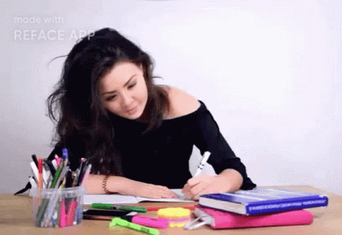 A Woman Is Sitting At A Desk Writing In A Notebook Surrounded By Books And Pens . GIF