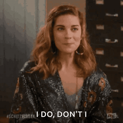 A Woman Is Sitting At A Table And Smiling While Holding Her Hair . GIF